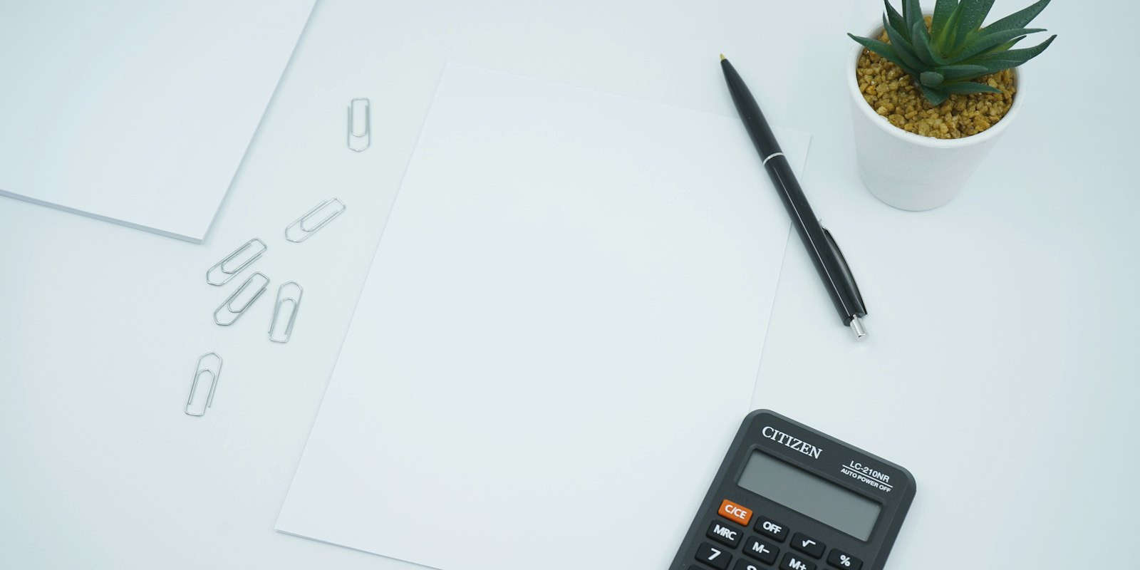A calculator, a pen and paper on a desk