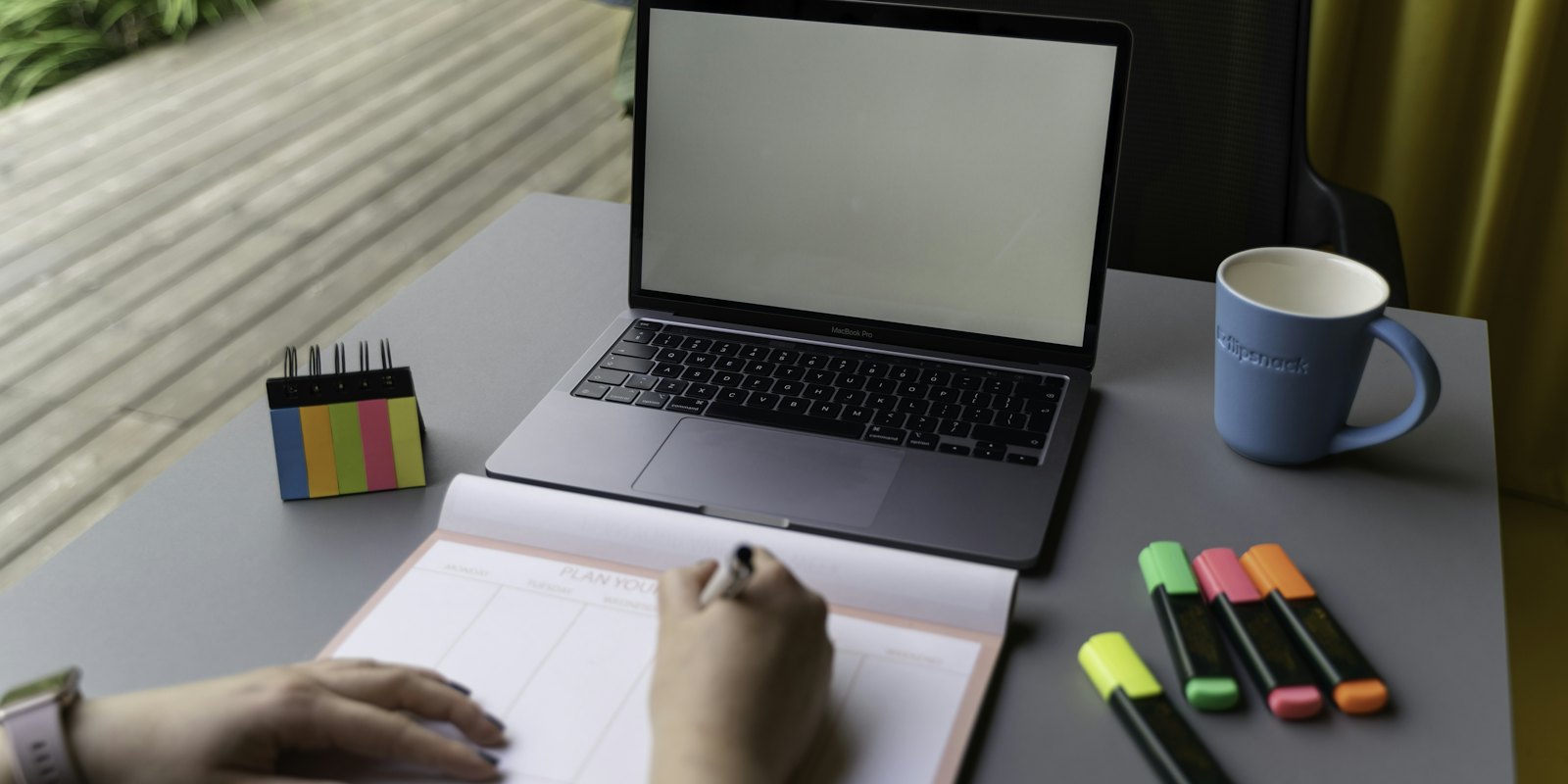 Someone writing in a notebook beside a laptop